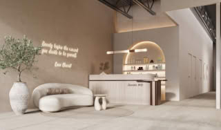 Minimalist beauty salon lounge with curved sofa, decorative plant, illuminated Coco Chanel quote, and modern reception counter.